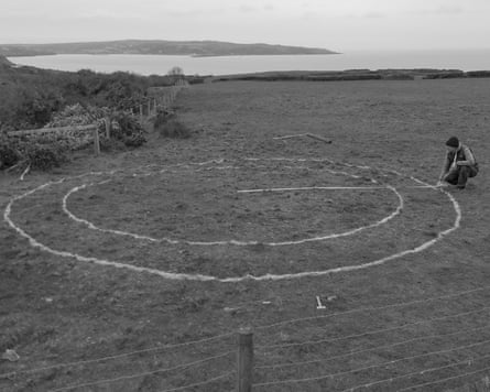 Mike Perry kneels, measuring concentric circles marked in a field overlooking the sea