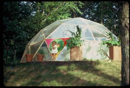 A toddler stands in front of a geodesic dome surrounded by plant pots.