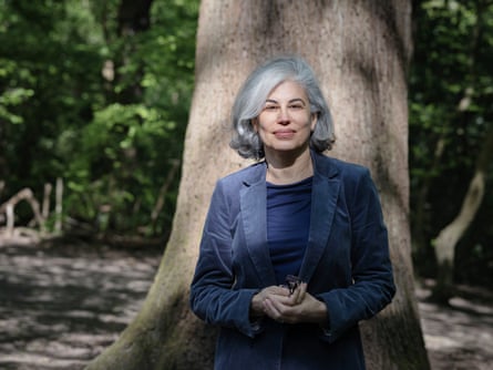 A woman in blue corduroy jacket and dark blue jeans leaning against a tree and looking at the camera