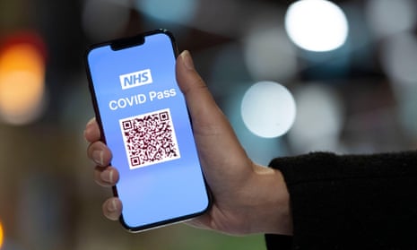 A close-up of a NHS COVID 19 pass in the hands of a woman against a blurred background at night.2H3T1GH A close-up of a NHS COVID 19 pass in the hands of a woman against a blurred background at night.