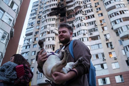 A man carries his dog in front of a residential multi-storey building damaged after a Russian drone strike on Kyiv.
