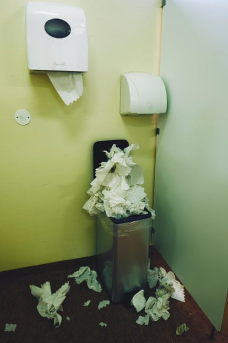A restroom paper towel dispenser, hand dryer and an over full bin