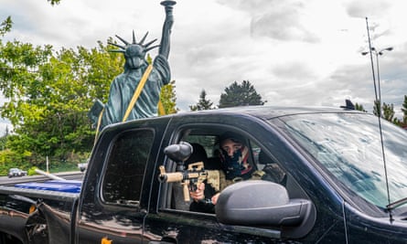 A member of the far-right group the Proud Boys aims a paintball gun while leaving a demonstration with a Statue of Liberty replica in the bed of the truck.