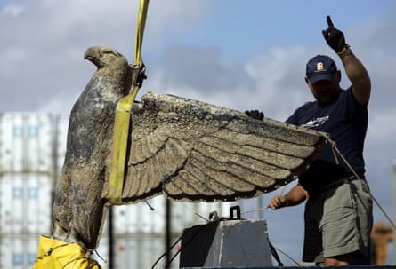 A eagle statue is hoisted up beside a person giving a hand gesture.