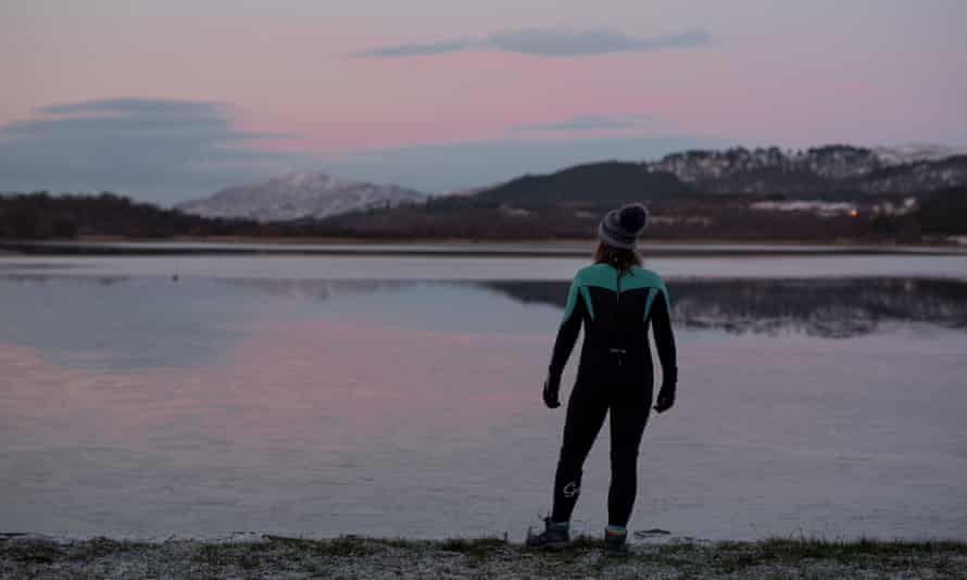 Man in a wetsuit and wolly hat by the side of a loch in Scotland at first light.
