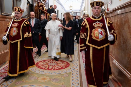 The pope walks down a corridor led by two men in ceremonial outfits