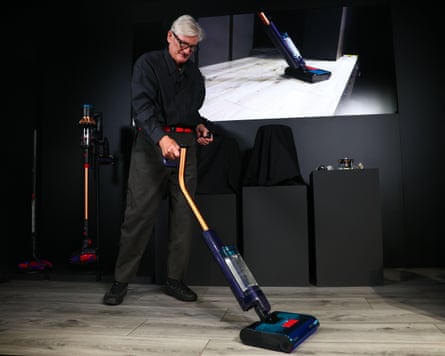 On an illuminated stage, Sir James Dyson demonstrates one of his vacuum cleaners