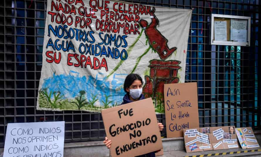 Una mujer que protesta contra el colonialismo frente a la embajada de España en la Ciudad de México sostiene un cartel que dice