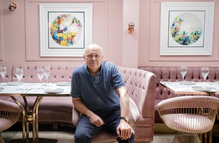 Sir Iain Duncan Smith faces the camera in a restaurant with pink banquette seating and pink walls