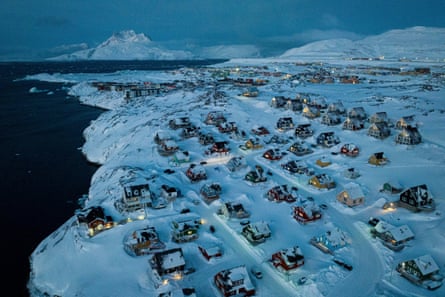 Houses covered in snow next to the sea with a mountain in the background