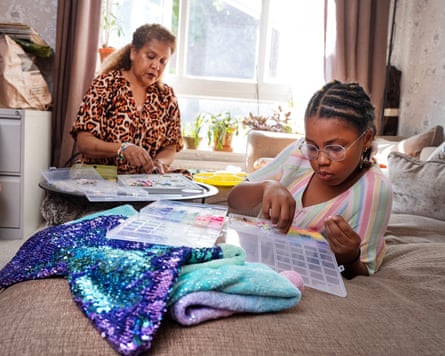 A grandmother sitting at a table and her granddaughter lying on the couch, they are both playing with arts and crafts