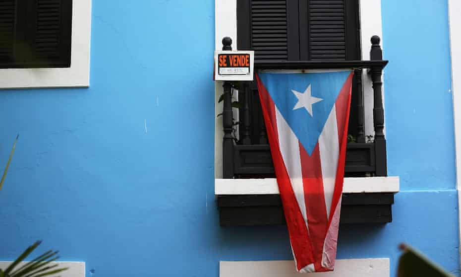 A for sale sign is seen hanging from a balcony next to a Puerto Rican flag in Old San Juan
