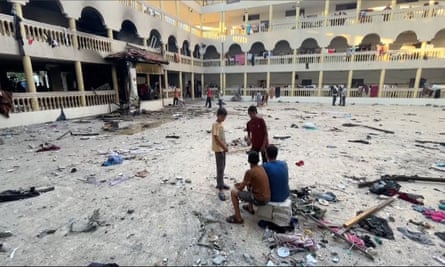 People sit in the yard of the school with debris strewn about