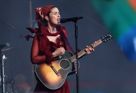 Gracie Abrams wearing a burgundy bandana, as she performs on stage with a guitar