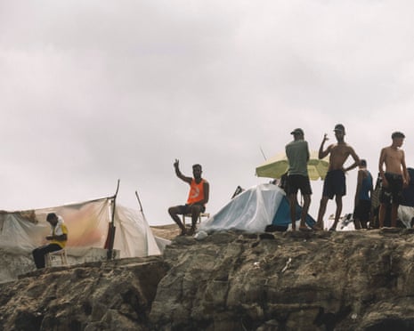 Young migrants stand on the rocks of a makeshift settlement on the coast of Ceuta.