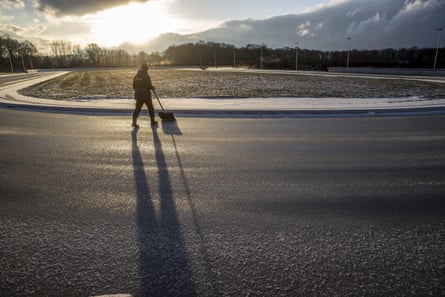 The silhouette of a person with a snow shovel on an outdoor rink