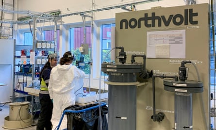 Employees at the Northvolt facility in Västerås; one woman wears white coveralls and another a visor-style face covering as they look at technical equipment
