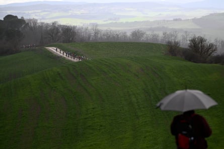 A fan watches the riders in the distance from under an umbrella.