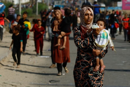 A woman carries a child while Palestinians fleeing north Gaza move southward as Israeli tanks roll deeper into the enclave.
