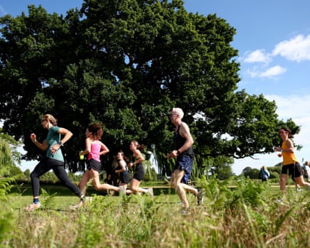 Runners jog through Bushy Park beneath a large tree on a sunny day during parkrun.