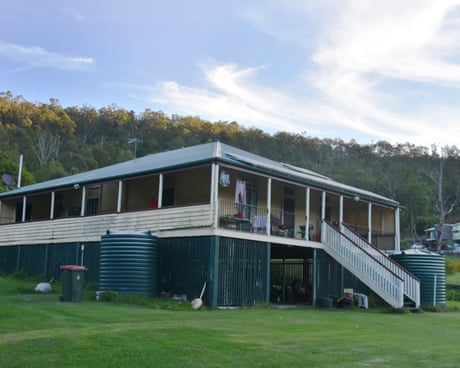 A Queenslander-style bungalow on a neat lawn with many trees in the background