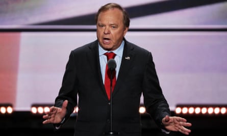 Middle-aged older white man wearing suite speaks and gestures on what appears to be a very large stage.