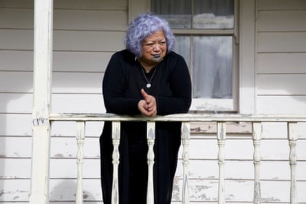 A woman with purple hair and a turquoise tattoo leans against a porch railing 