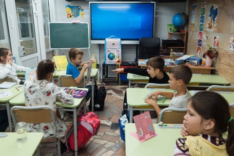 Six young children sit at tables in a classroom