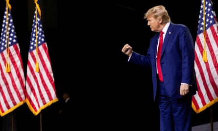 a man in a blue suit with a red tie holds up his fist near three american flags