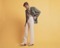 Stephen Libby wears a dark beige blazer with brooch, a beige shirt, striped tie, cream trousers and white heeled boots