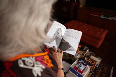 A shot over the shoulder of a woman reading a book, open at an illustration of a woman