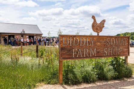 Wooden sign with hen on top and the words ‘Diddly Squat Farm Shop’, with people queueing up in backdrop to enter building.