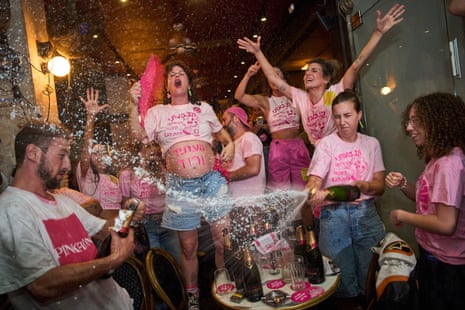 Israelis in pink t-shirts celebrate election results, spraying sparkling wine indoors