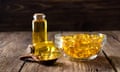 Golden-yellow fish oil tablets in a glass bowl, a spoon and bottled as a liquid on a wooden table