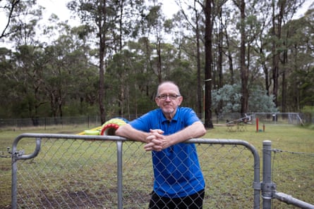 A man in a blue shirt leaning on an iron fence in a large suburban back yard.