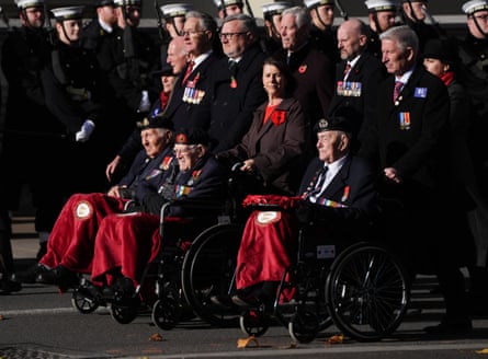 Three veterans in uniform are pushed in wheelchairs along Whitehall during the march past