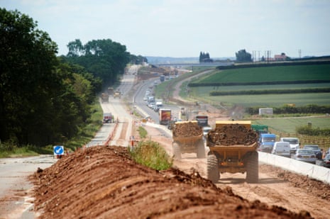 Large dump trucks carrying soil work on the A46 road construction site with traffic diverted alongside