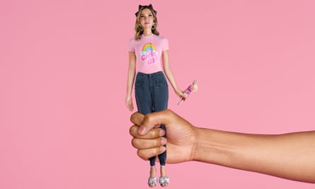 Jess Cartner-Morley wearing navy trousers and a Girly Girl T-shirt, styled as a doll being held in a hand