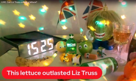 A small table crowded with items, including a number of items of produce with googly eyes pasted on, yellow and green lights, the Union Jack flag of the UK, and a digital timer.