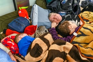 A frightened cat looks up from between two children sleeping on a camp bed at Kraków train station