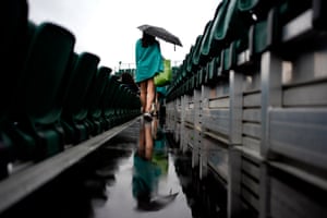 Low-down shot of rain between two rows of seats, as a woman walks away carrying an umbrella and a shopping bag