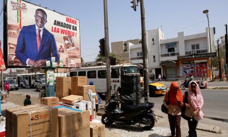 People walk past an electoral billboard of candidate Amadou Ba of President Macky Sall's ruling coalition, in a street in Dakar