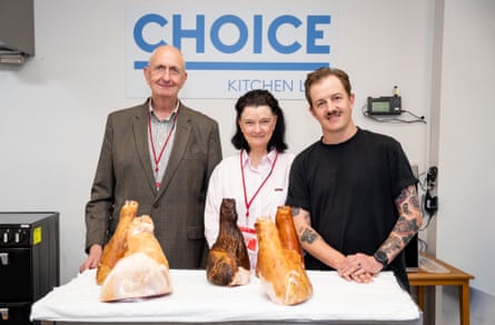 Three people standing in front of a table of ham legs