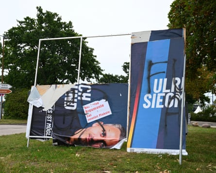 A vandalised campaign banner of AfD candidate Ulrich Siegmund, spray-painted and torn, stands on grass. A vandalised campaign banner of AfD candidate Ulrich Siegmund, spray-painted and torn, stands on grass.