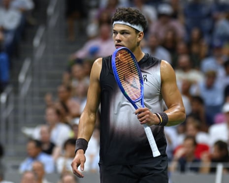 Ben Shelton holds his racket near his face, looking off to the side during a match