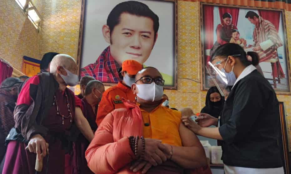 A health worker inoculates a dose of a COVID-19 coronavirus vaccine to a Buddhist monk sitting in front of a portrait of Bhutan’s King Jigme Khesar Namgyel Wangchuck (top C) during the first day of vaccination in Bhutan, at Lungtenzampa Middle Secondary school in Thimphu.