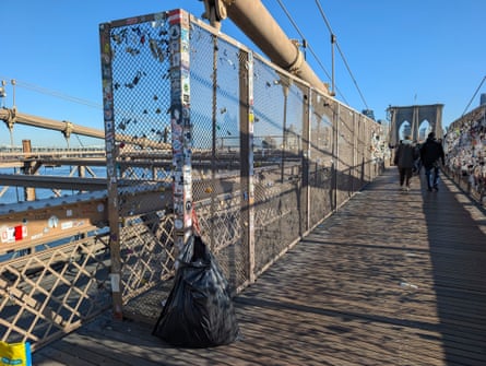 A full trash bag next to a mostly cleared section of fencing on the Brooklyn Bridge