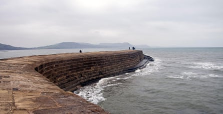 A curving stone harbour wall snakes out into a grey sea.