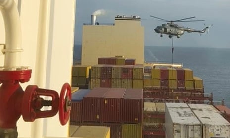A helicopter flying low over a container ship