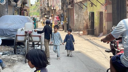 A young boy and girl walk past a man with a tricycle loaded with water butts on a bustling street in India.